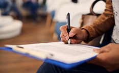 Hands holding pen filling out paperwork on blue clipboard in waiting room