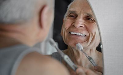 Man holding a toothbrush and smiling in bathroom mirror