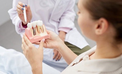Dentist pointing at a dental implant model that a patient is holding