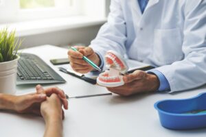 Dentist's hands pointing to model teeth with pen discussing treatment with patient