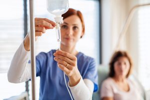 Woman in blue scrubs adjusting IV sedation with patient blurry in background